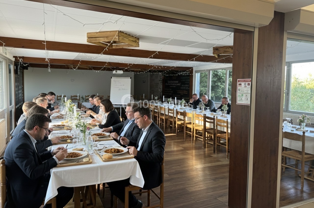 Des personnes en tenue formelle dînent autour de longues tables dans une salle lumineuse avec des décorations simples.