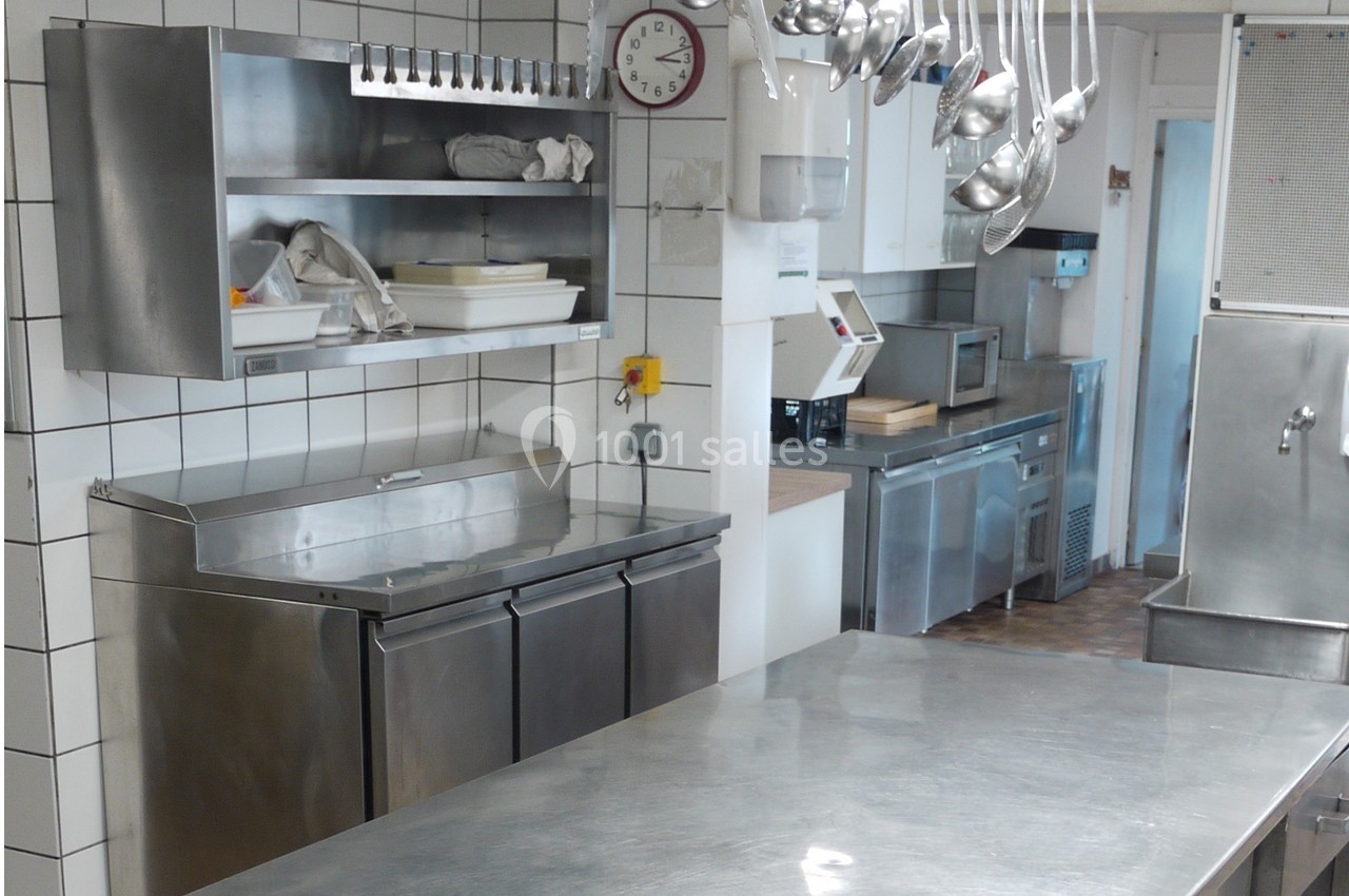 Cuisine professionnelle avec plans de travail en acier inoxydable, équipements de cuisson et ustensiles suspendus.