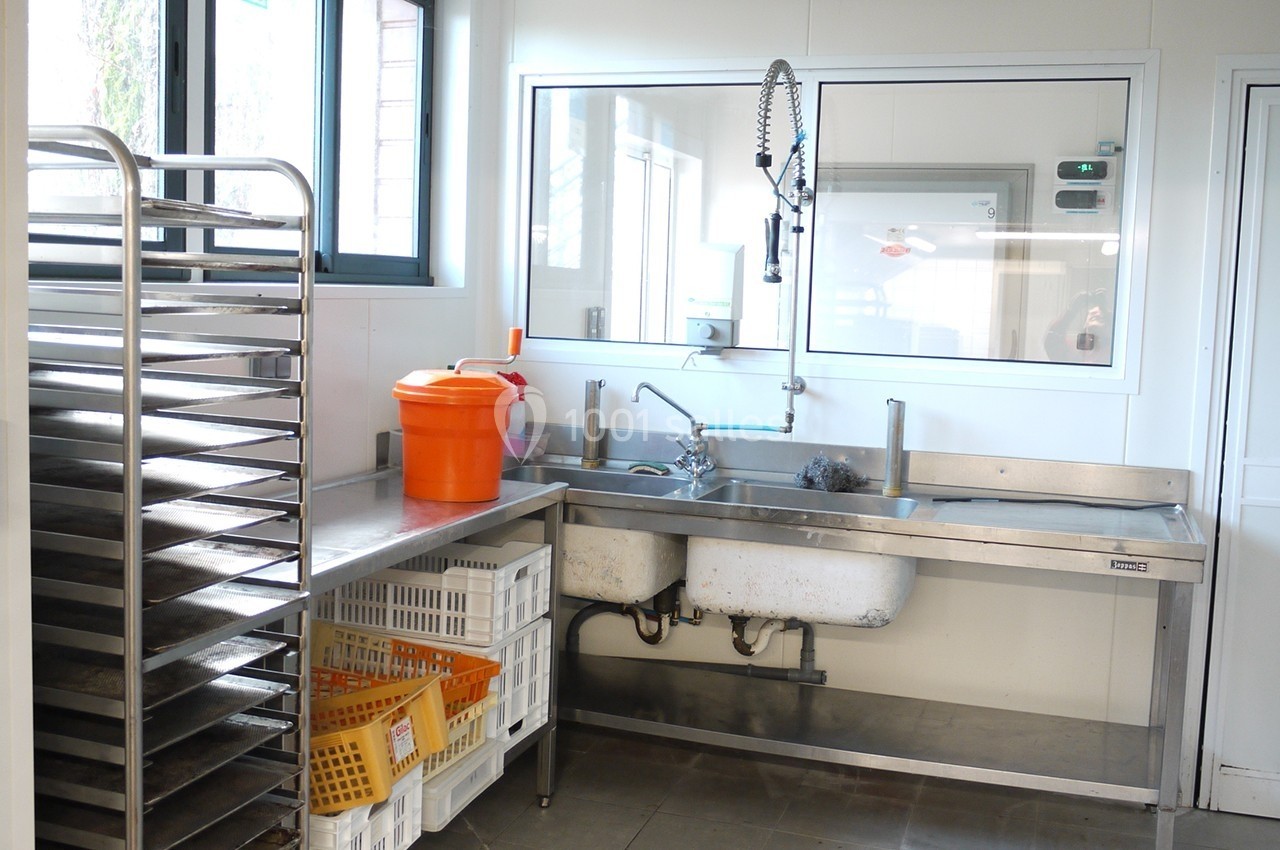Évier en inox avec robinet flexible dans une cuisine professionnelle, entouré de paniers et d'étagères métalliques.
