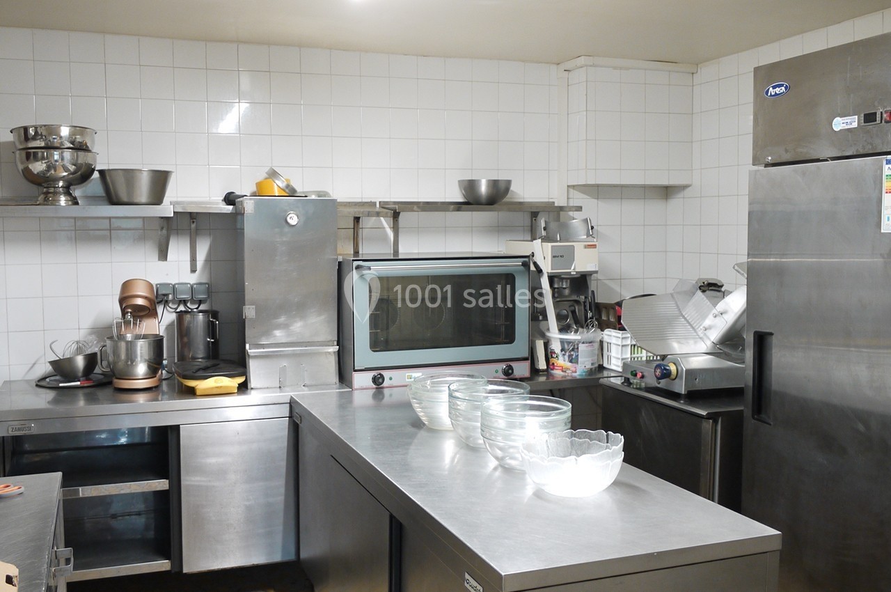 Cuisine professionnelle équipée avec plans de travail en inox, four, réfrigérateur et divers ustensiles.