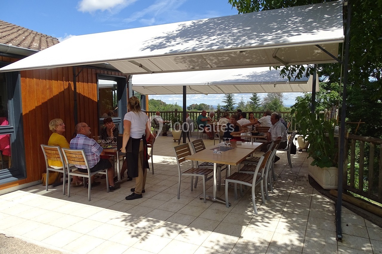 Terrasse ombragée avec des tables occupées par des personnes en train de discuter et une serveuse en service.