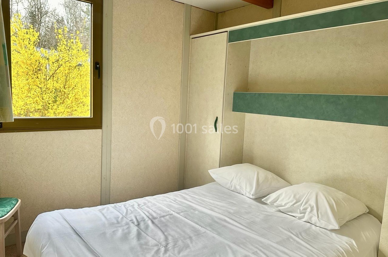 Lit double avec draps blancs dans une chambre lumineuse, fenêtre donnant sur un arbre en fleurs jaunes.