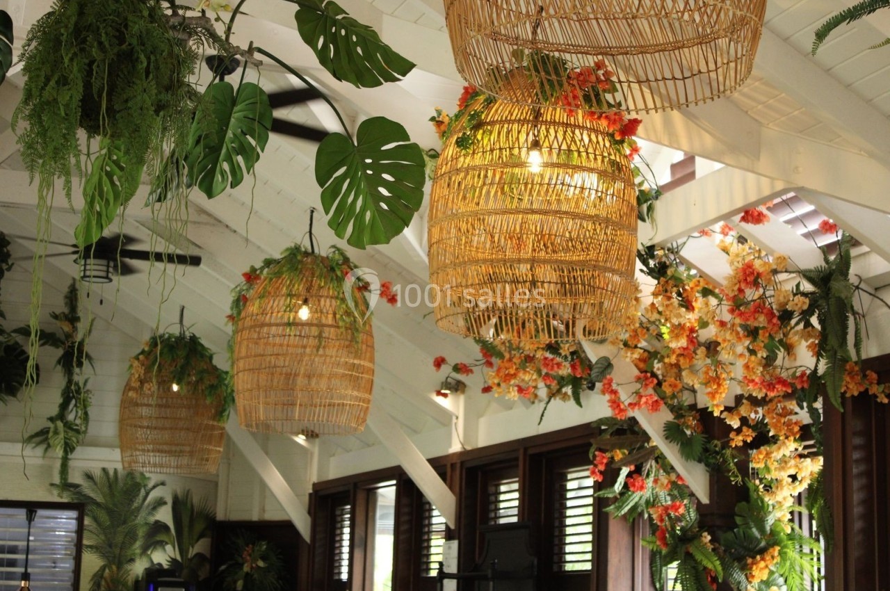 Suspensions en rotin illuminées dans un intérieur tropical avec plantes vertes et fleurs colorées.