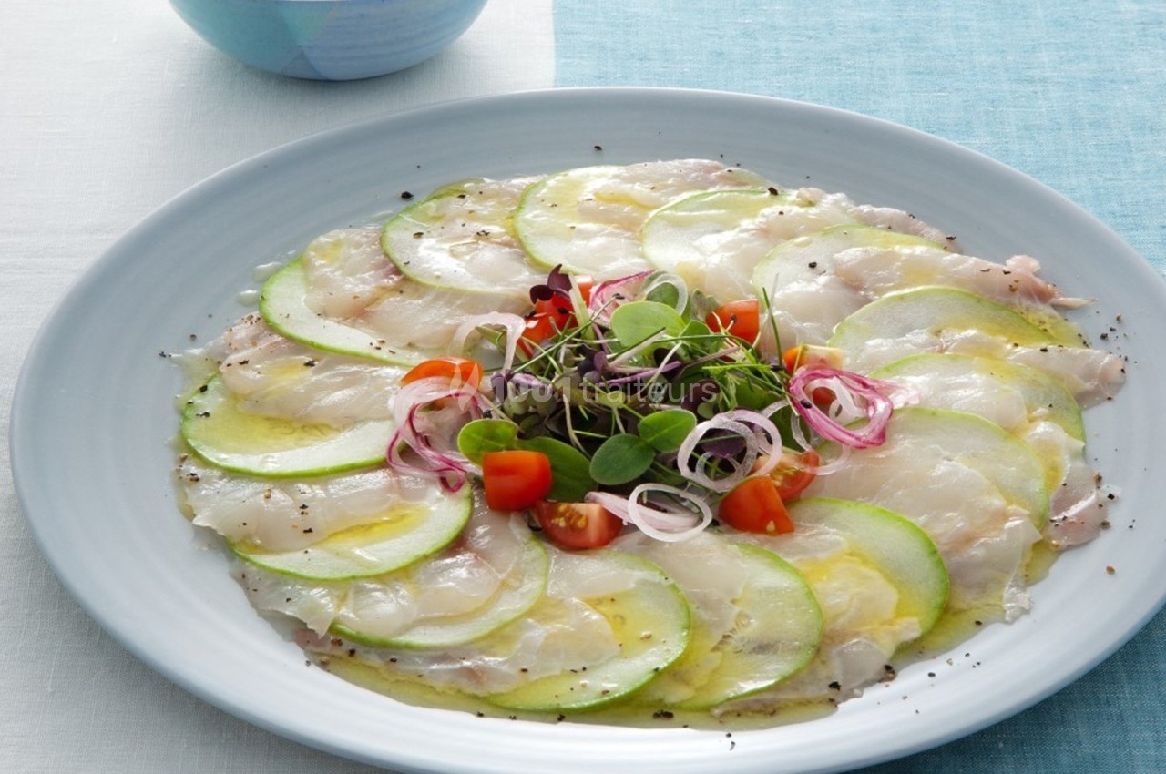 Assiette de carpaccio de poisson blanc avec tranches de courgette, tomates cerises, oignons rouges et jeunes pousses.