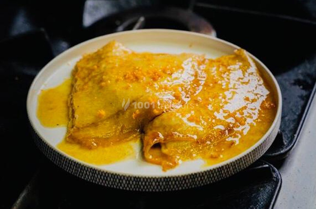 Crêpes nappées de sauce dorée servies dans une assiette blanche sur une cuisinière sombre.