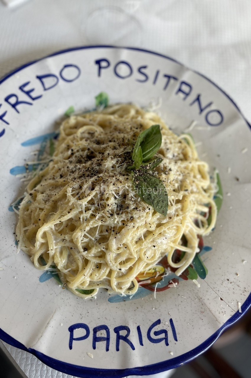 Assiette de pâtes crémeuses garnies de basilic, poivre et parmesan, servie dans une assiette décorative.