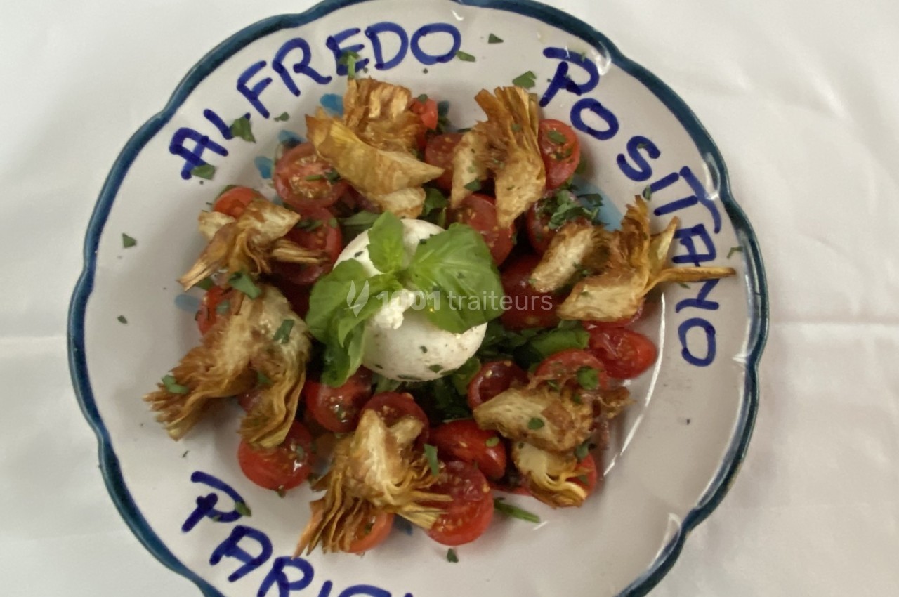 Assiette de salade composée de tomates cerises, burrata, artichauts grillés et basilic, présentée sur une assiette décorée.