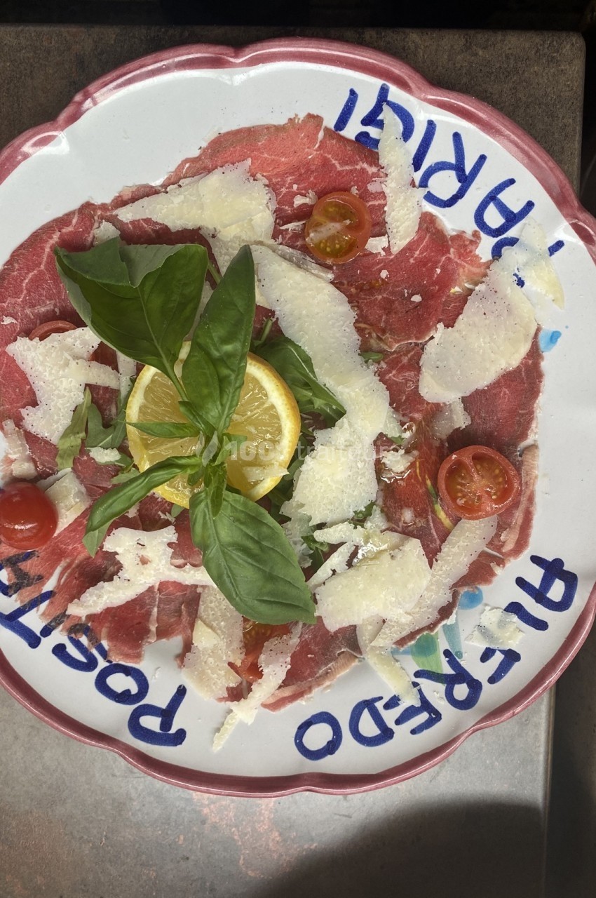 Assiette de carpaccio de bœuf garnie de parmesan, tomates cerises, basilic et tranche de citron.