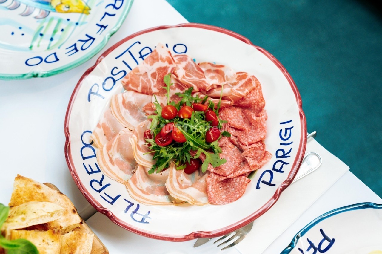Assiette de charcuterie italienne avec jambon, salami, roquette et tomates cerises, servie sur une table dressée.