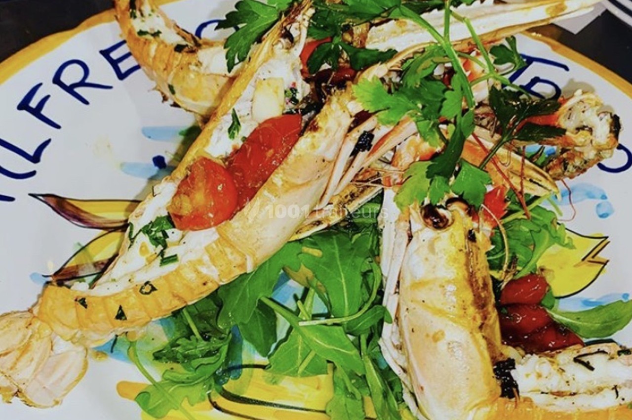 Assiette de langoustines grillées servies sur un lit de roquette avec tomates cerises et herbes fraîches.