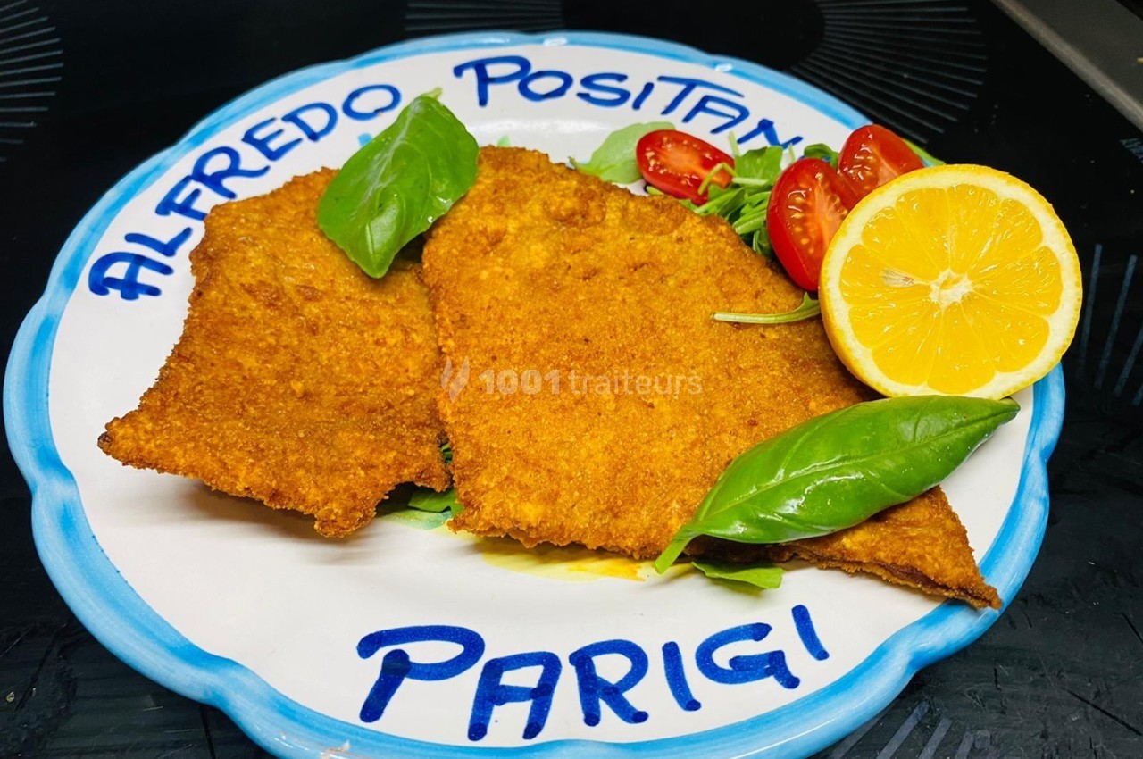 Assiette contenant deux escalopes panées garnies de basilic, tomates cerises et un demi-citron.