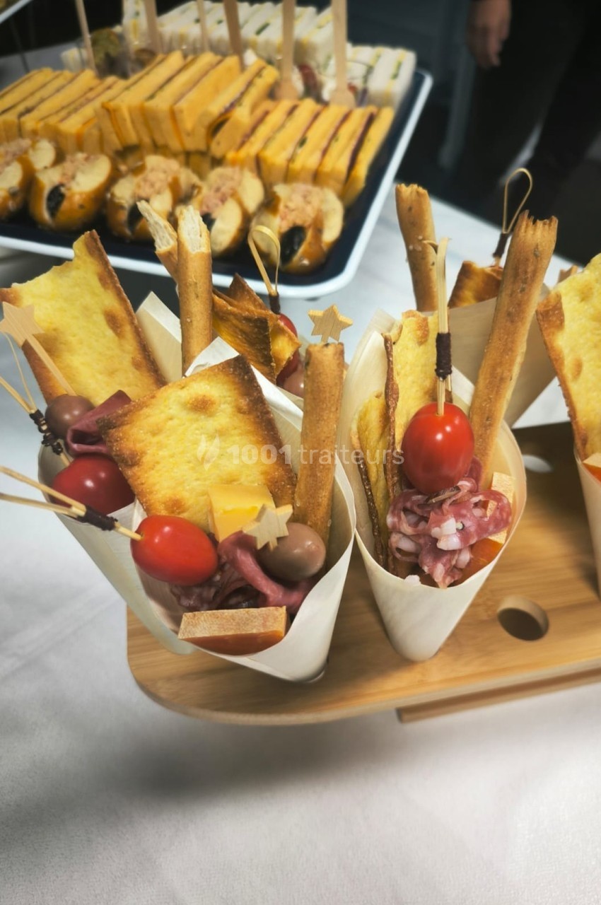 Cônes apéritifs garnis de gressins, tomates cerises, charcuterie et toasts, présentés sur un plateau en bois.