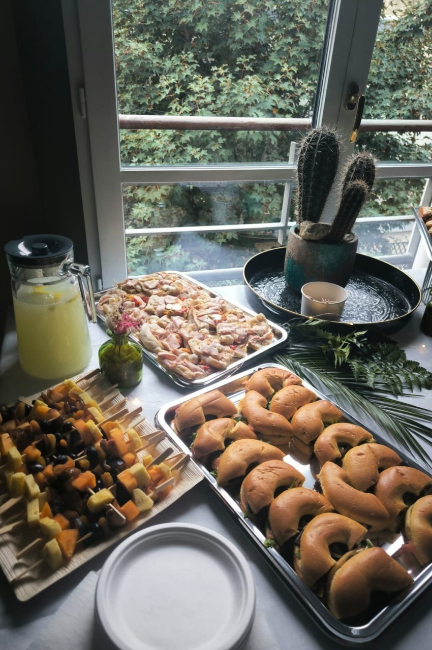 Buffet composé de mini-sandwichs, brochettes de fruits, pizzas et limonade, disposé près d'une fenêtre avec vue sur des…