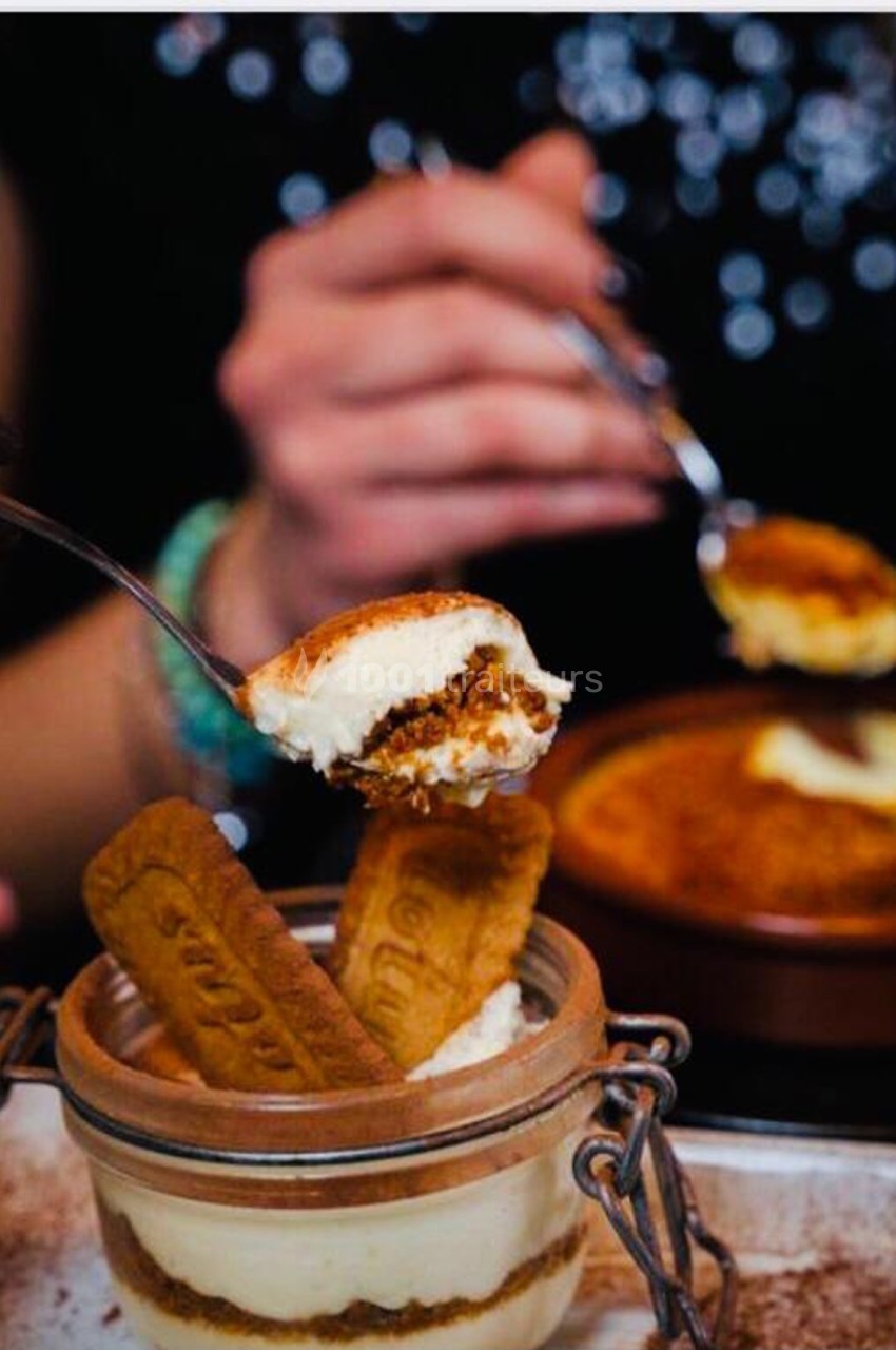 Deux personnes dégustent des desserts, dont un tiramisu en pot décoré de biscuits spéculoos.
