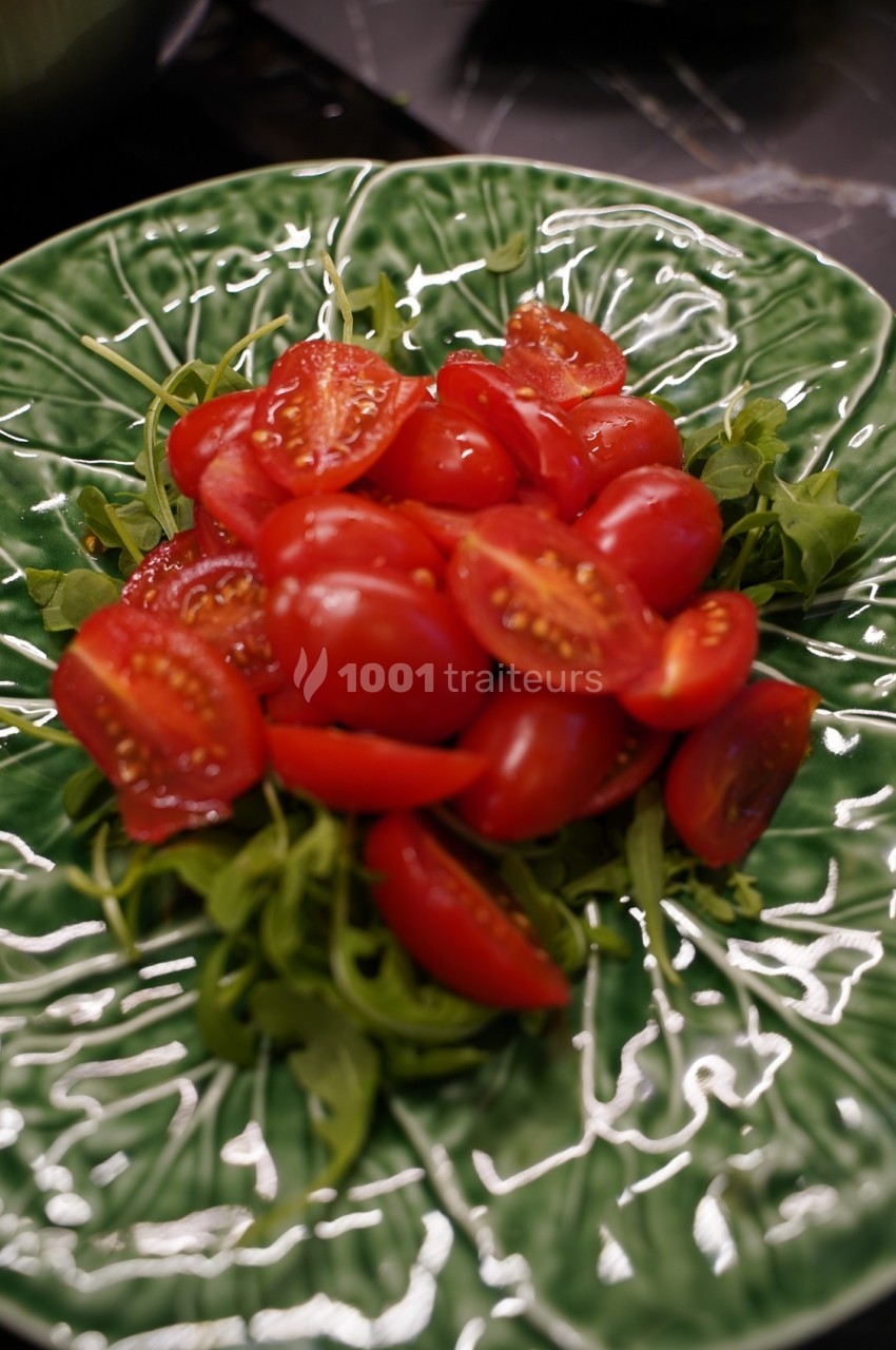 Salade de roquette garnie de tomates cerises coupées en deux, servie dans une assiette verte texturée.