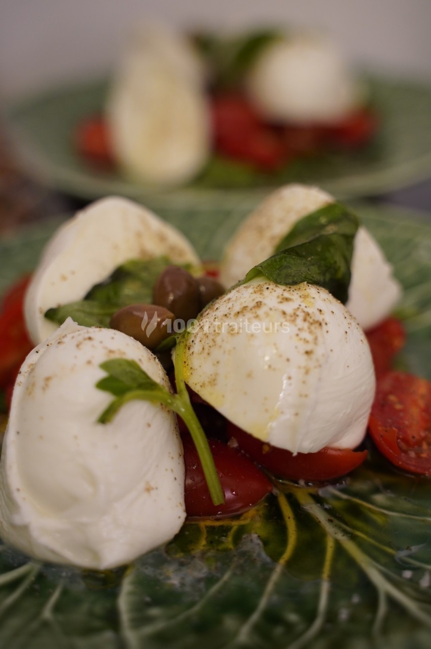Assiette de salade caprese avec mozzarella, tomates, olives, basilic et assaisonnement, servie sur une feuille décorative.