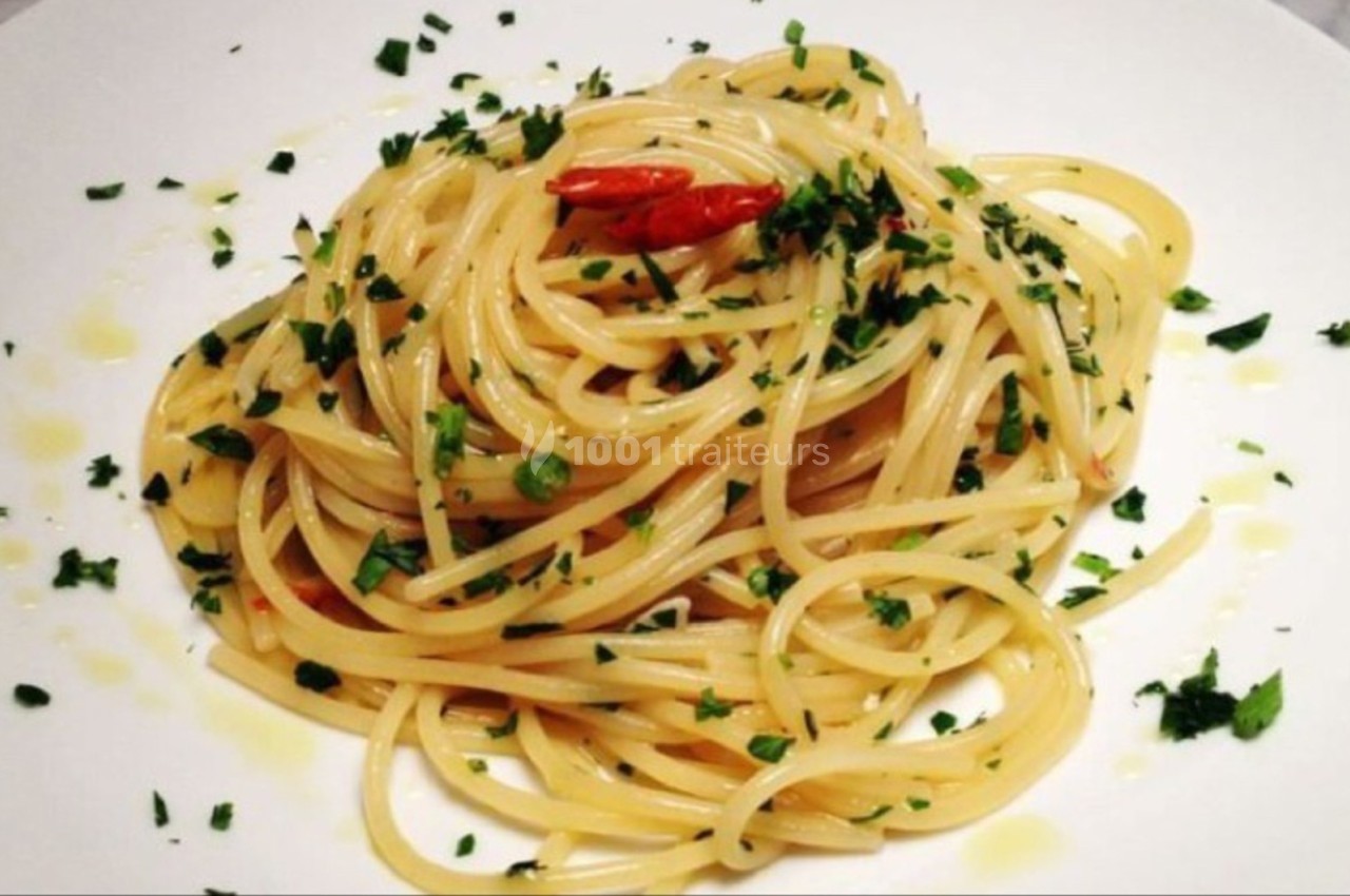 Assiette de spaghetti assaisonnés à l'huile d'olive, piment et persil, présentée sur une table blanche.