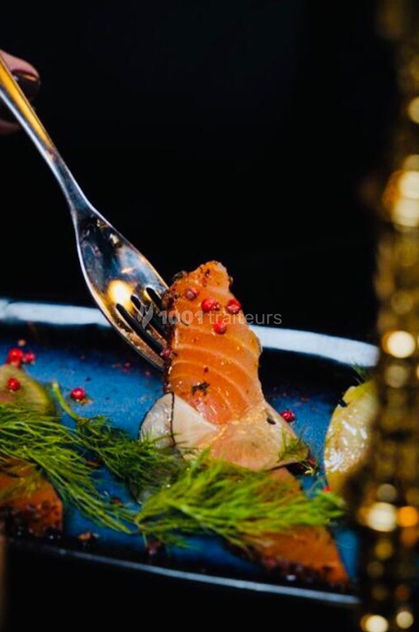 Tranche de saumon fumé garnie d'aneth, baies roses et citron, servie sur une assiette bleue.