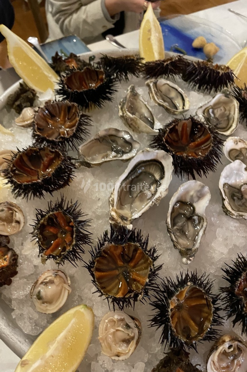 Plateau de fruits de mer avec oursins, huîtres, palourdes et quartiers de citron disposés sur de la glace.