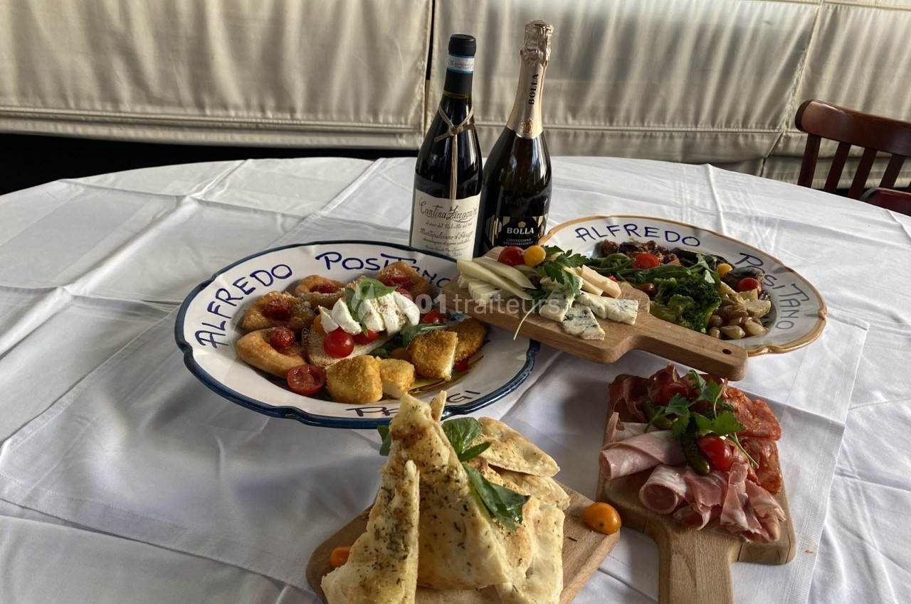 Assortiment de plats italiens avec charcuterie, fromages, légumes, pain et bouteilles de vin sur une table dressée.