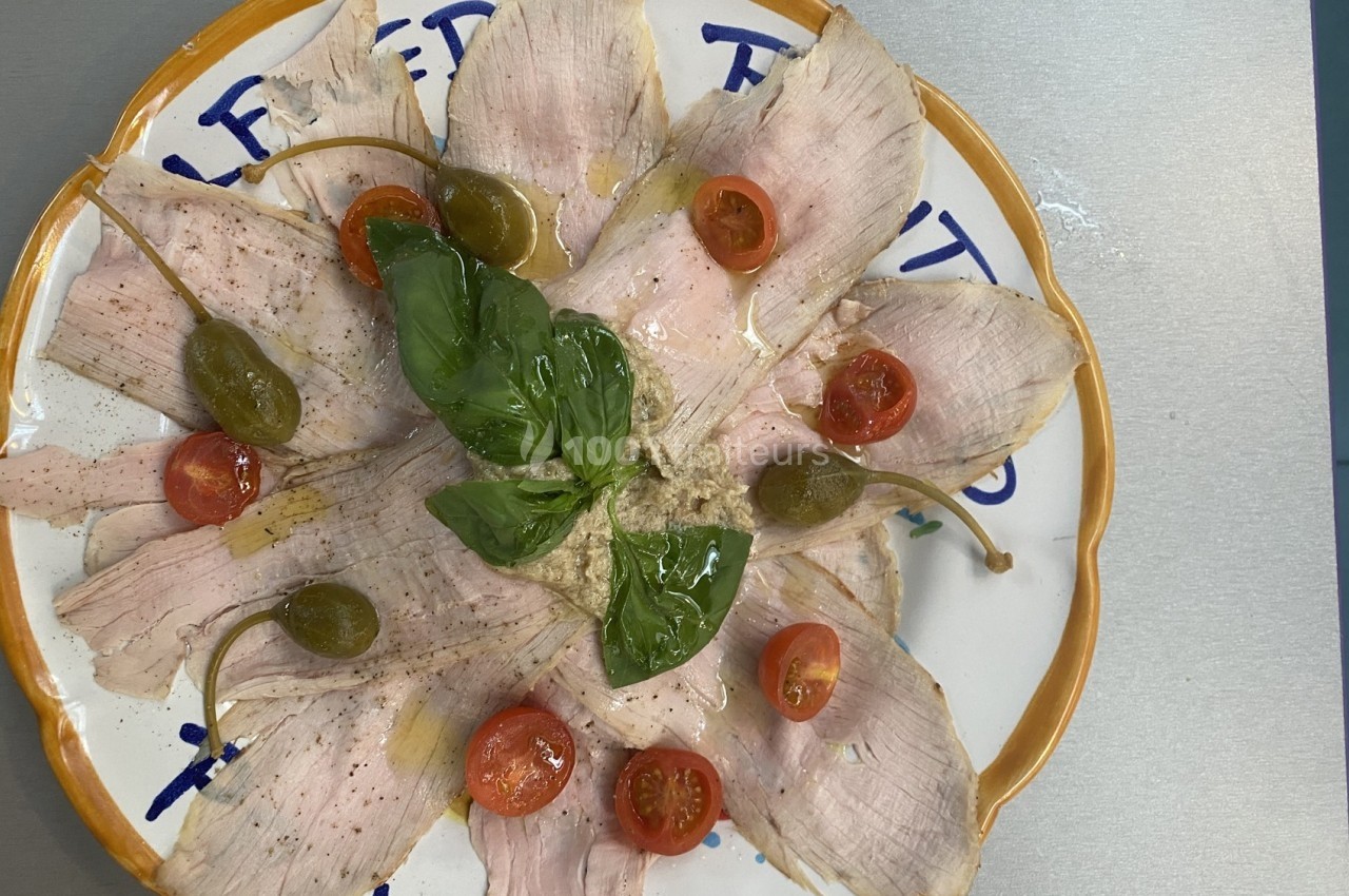 Assiette de vitello tonnato garnie de câpres, tomates cerises et feuilles de basilic.