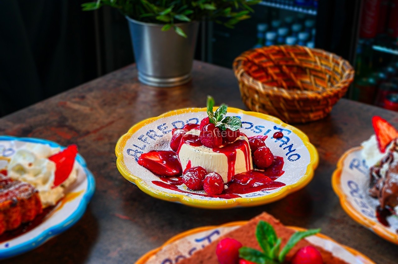 Assiette de dessert avec un cheesecake garni de fruits rouges et de menthe, posé sur une table en bois.