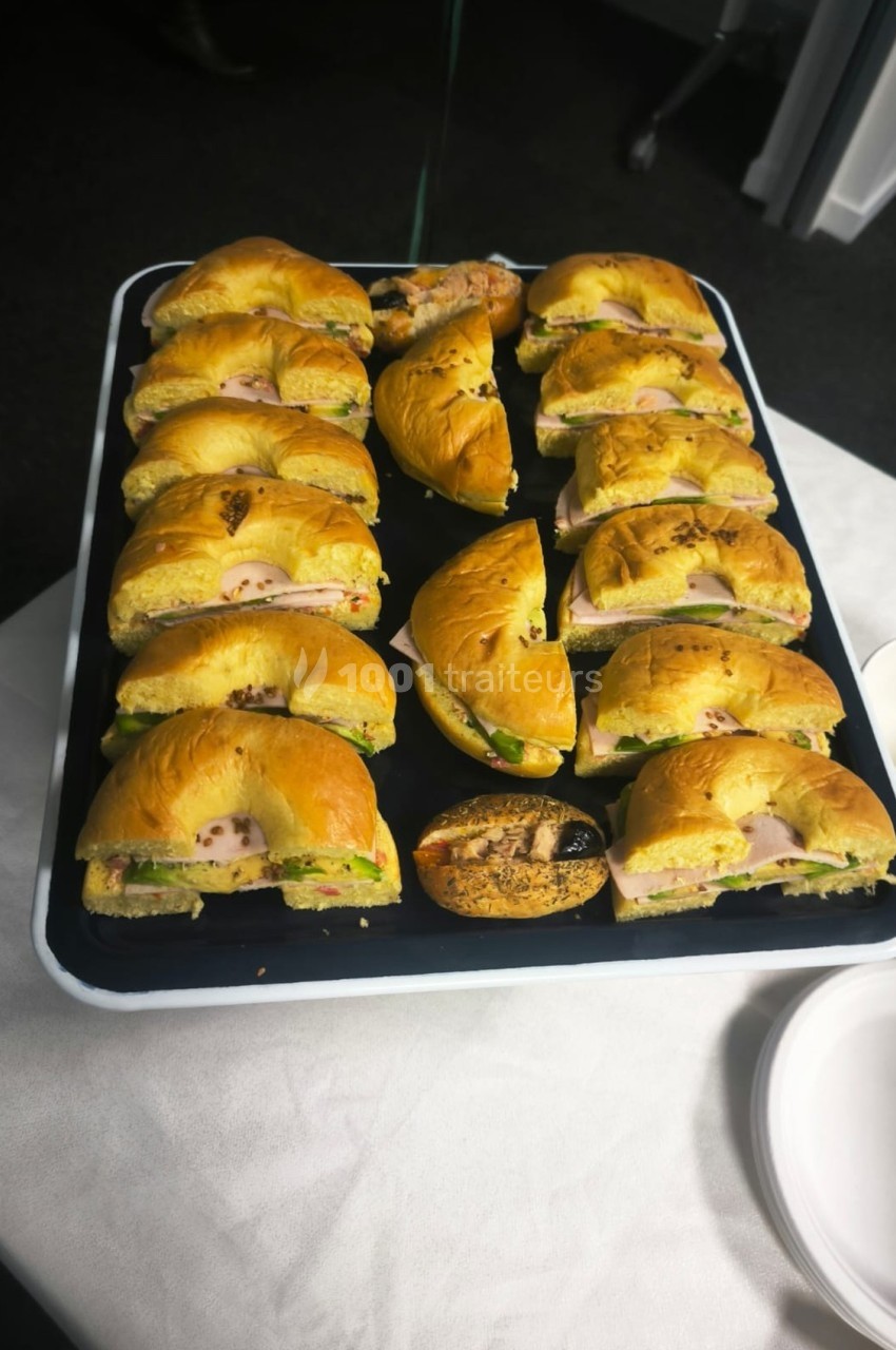 Plateau de bagels garnis de saumon, fromage frais et légumes, disposés sur une table blanche.