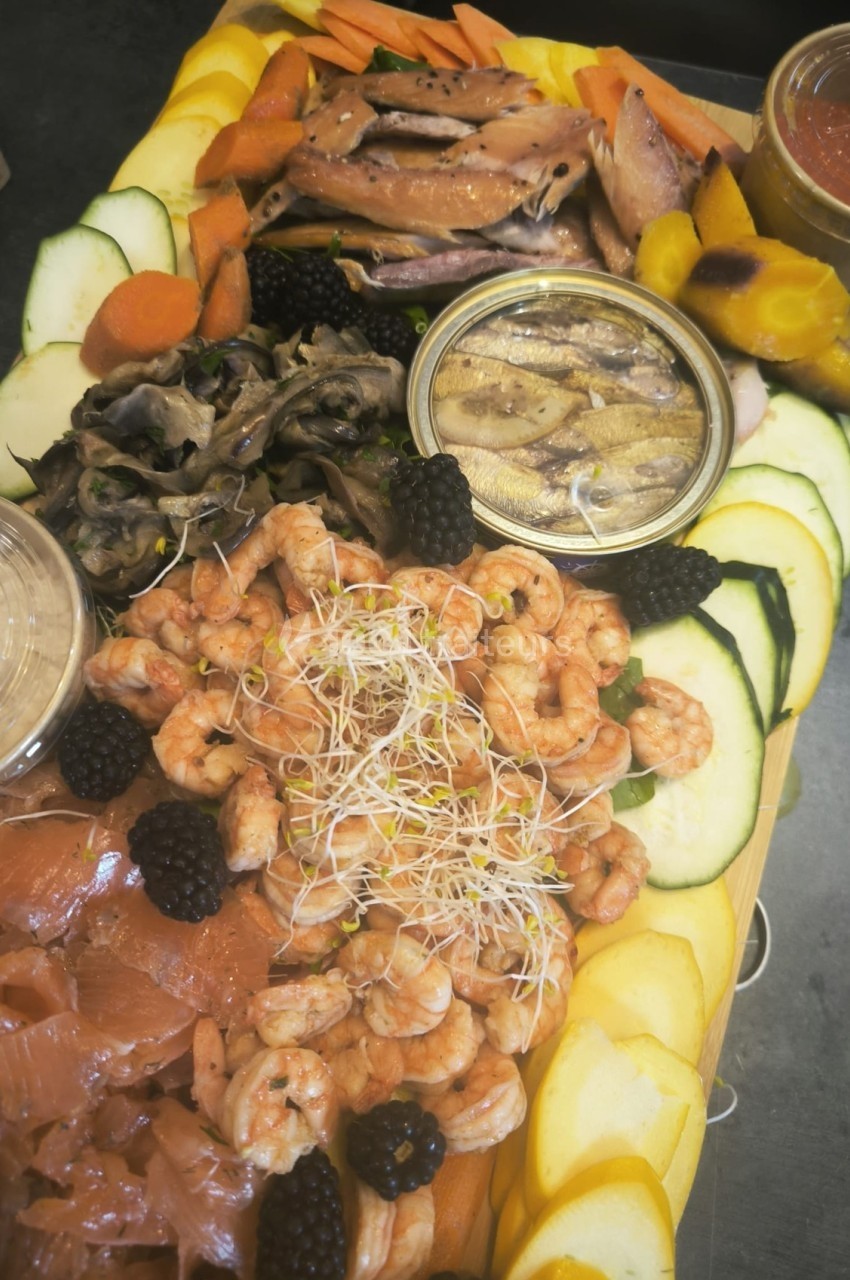 Plateau de fruits de mer avec crevettes, saumon fumé, anchois, légumes frais et condiments variés.