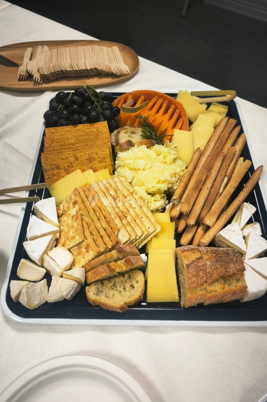Plateau de fromages variés avec crackers, pain, gressins, raisins et garnitures sur une table dressée.