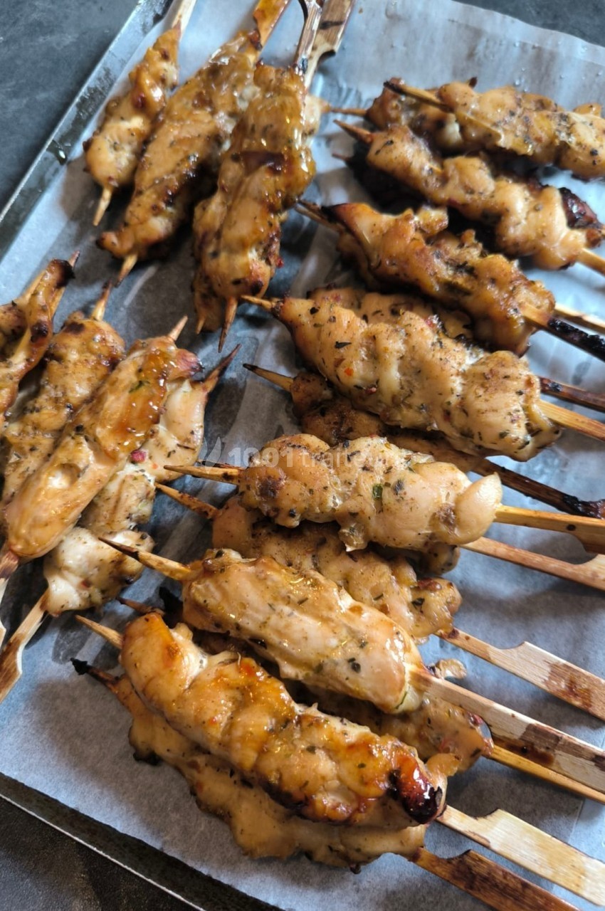 Brochettes de poulet grillées avec marinade dorée, disposées sur une plaque recouverte de papier sulfurisé.