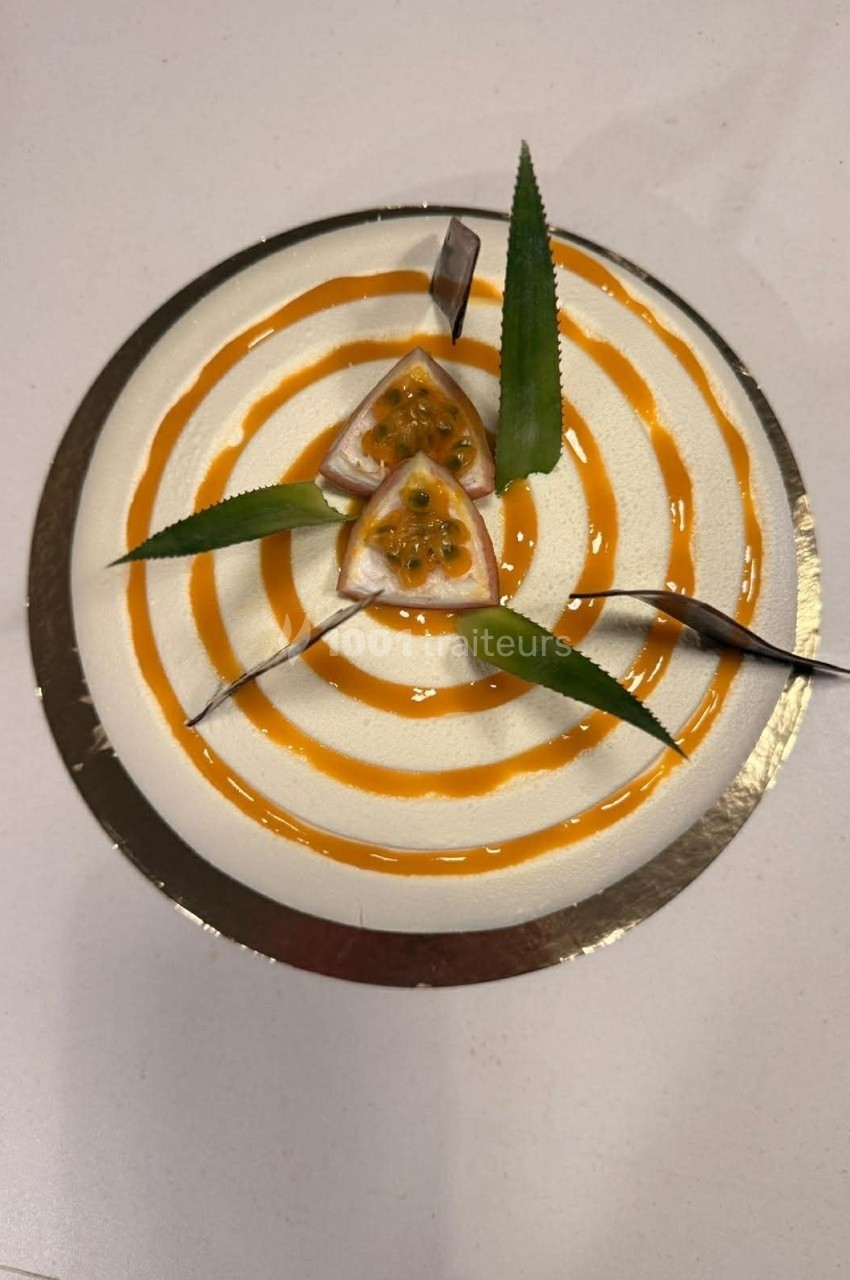 Gâteau rond décoré de spirales orange, tranches de fruit de la passion et feuilles vertes sur le dessus.