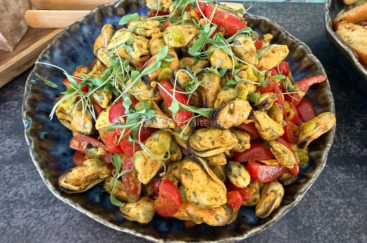 Assiette de moules marinées avec morceaux de poivrons rouges et herbes fraîches, présentée sur une table.