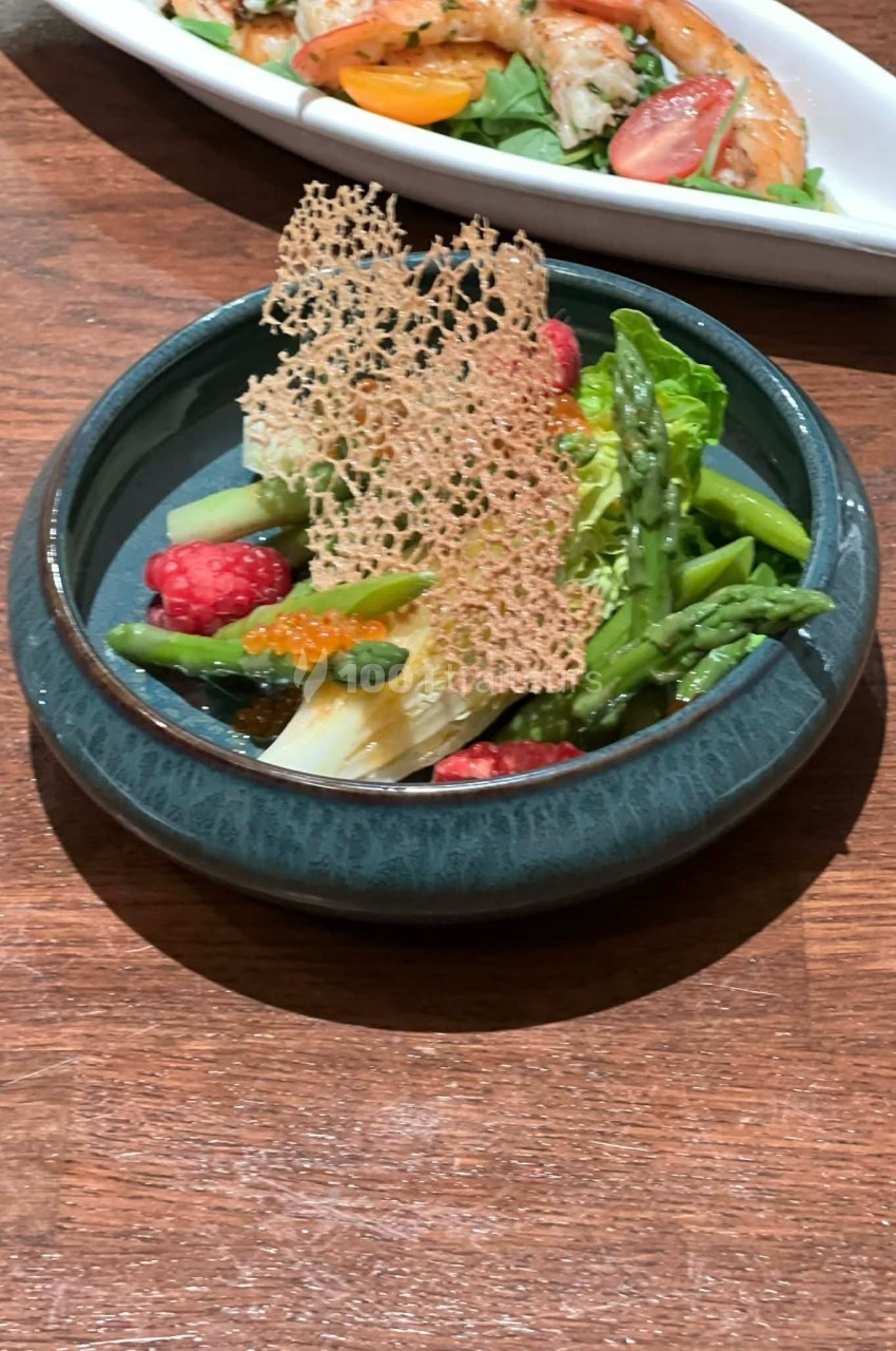 Assiette de légumes verts, framboises, œufs de poisson et tuile croustillante, présentée sur une table en bois.
