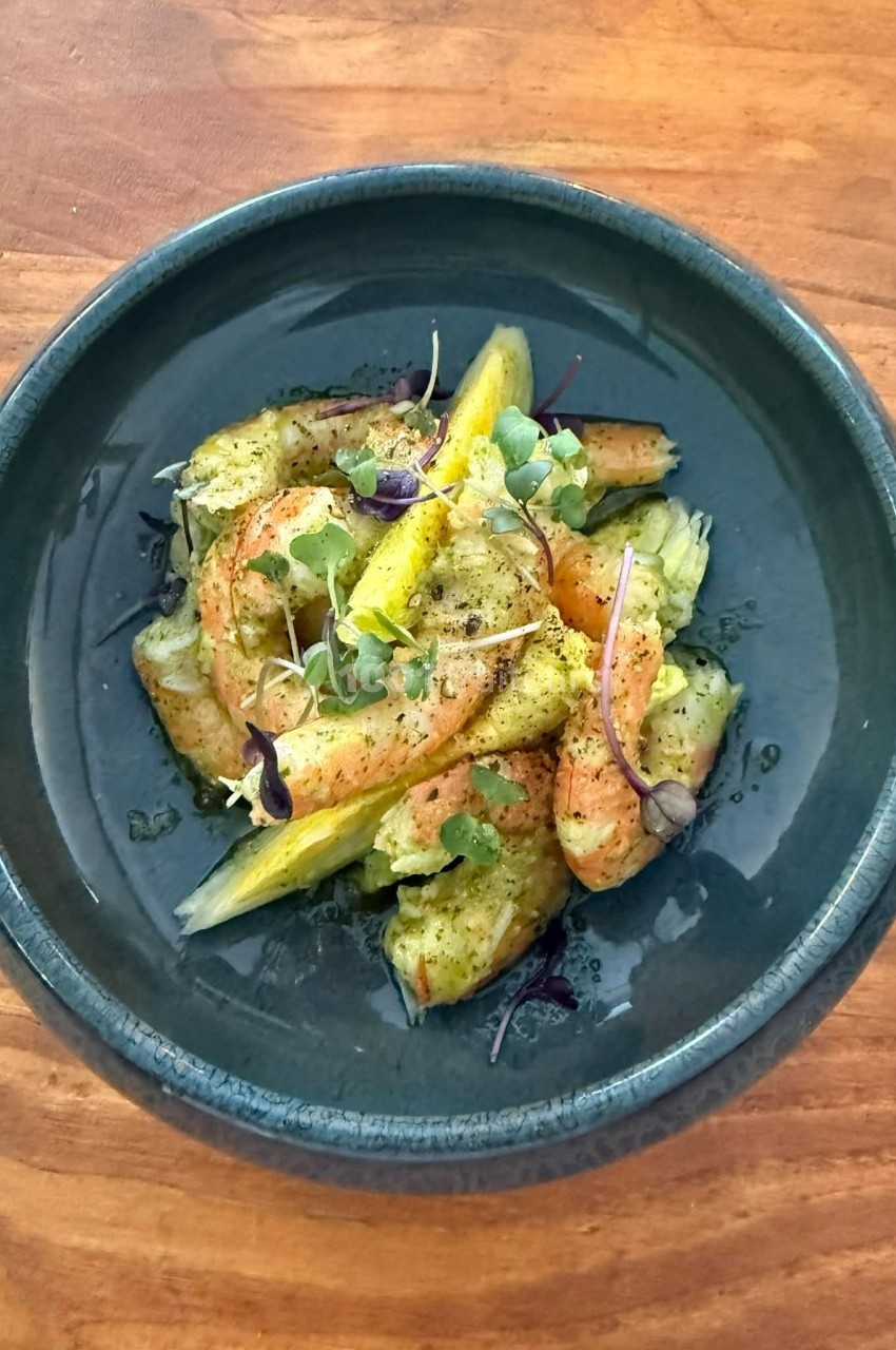 Assiette de crevettes marinées avec quartiers d'agrumes et micro-pousses, servie sur une table en bois.