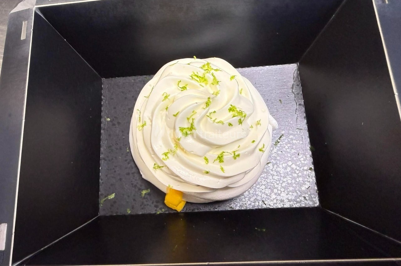 Mousse blanche décorée de zestes de citron vert, présentée dans un moule rectangulaire noir.