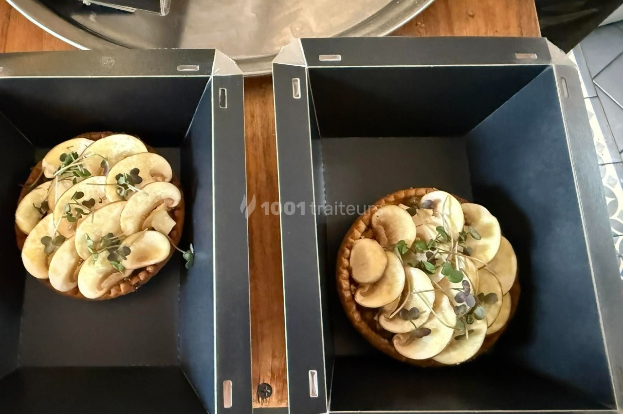 Deux tartes aux pommes garnies de micro-pousses, présentées dans des boîtes noires sur une table en bois.