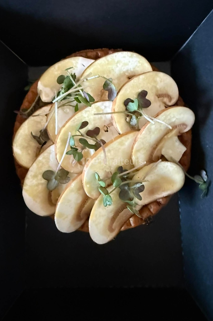 Tarte garnie de fines tranches de champignons frais et de jeunes pousses, présentée dans une boîte noire.