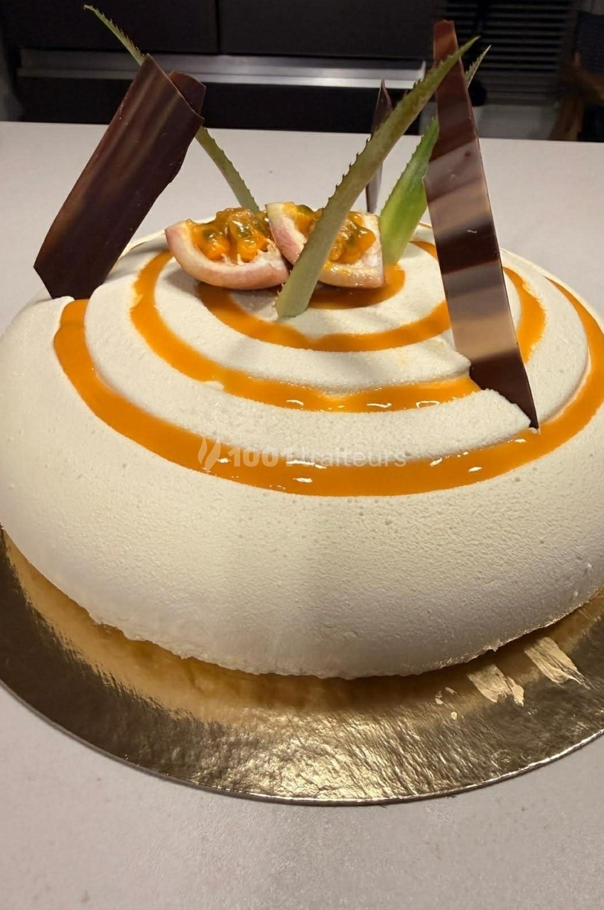 Gâteau rond décoré de spirales orange, morceaux de fruits de la passion, feuilles et plaques de chocolat.