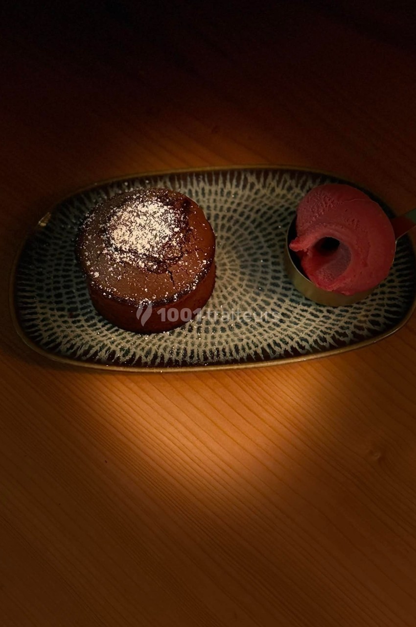 Dessert composé d'un fondant au chocolat saupoudré de sucre glace et d'une boule de glace rose sur une assiette.