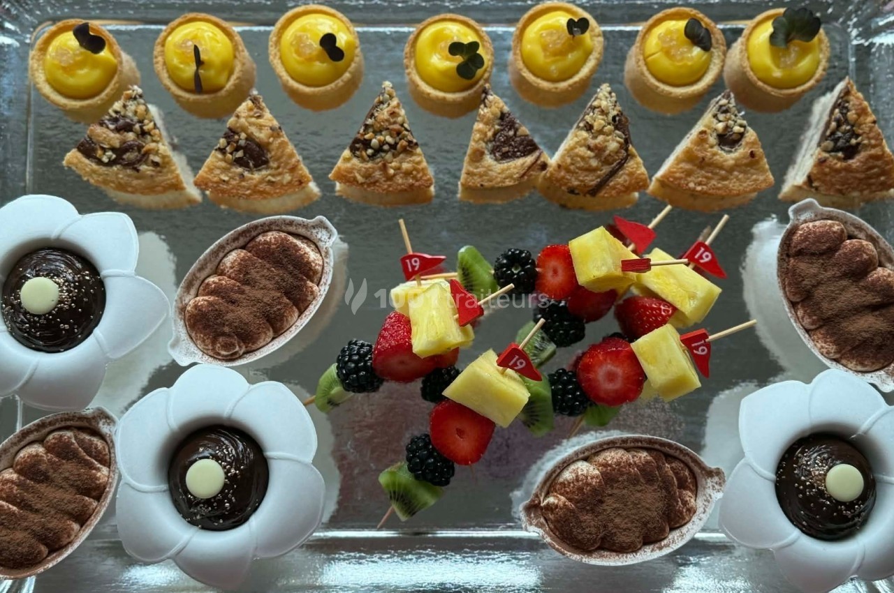 Plateau de desserts variés comprenant tartelettes, parts de gâteau, tiramisus et brochettes de fruits colorées.