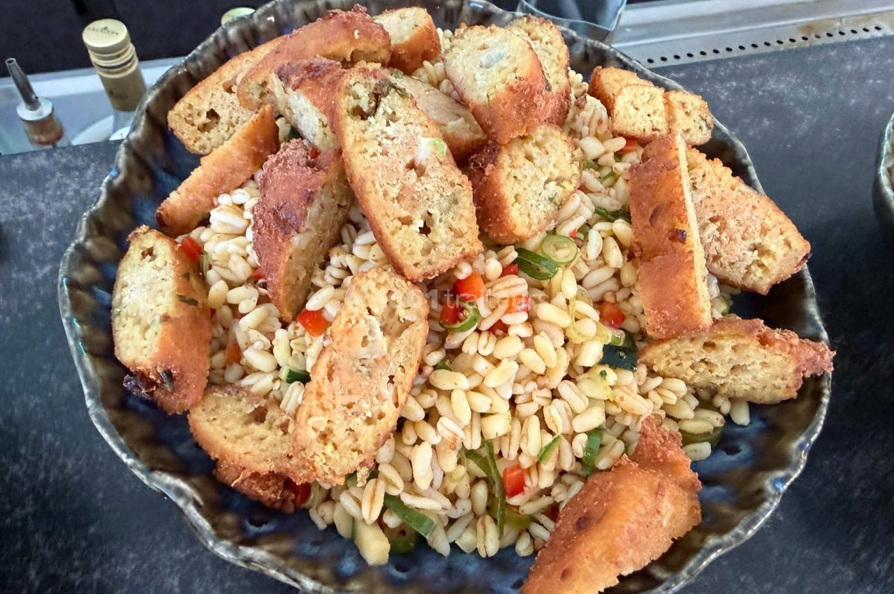 Salade de pâtes orzo avec légumes colorés et croûtons dorés dans un plat en céramique.
