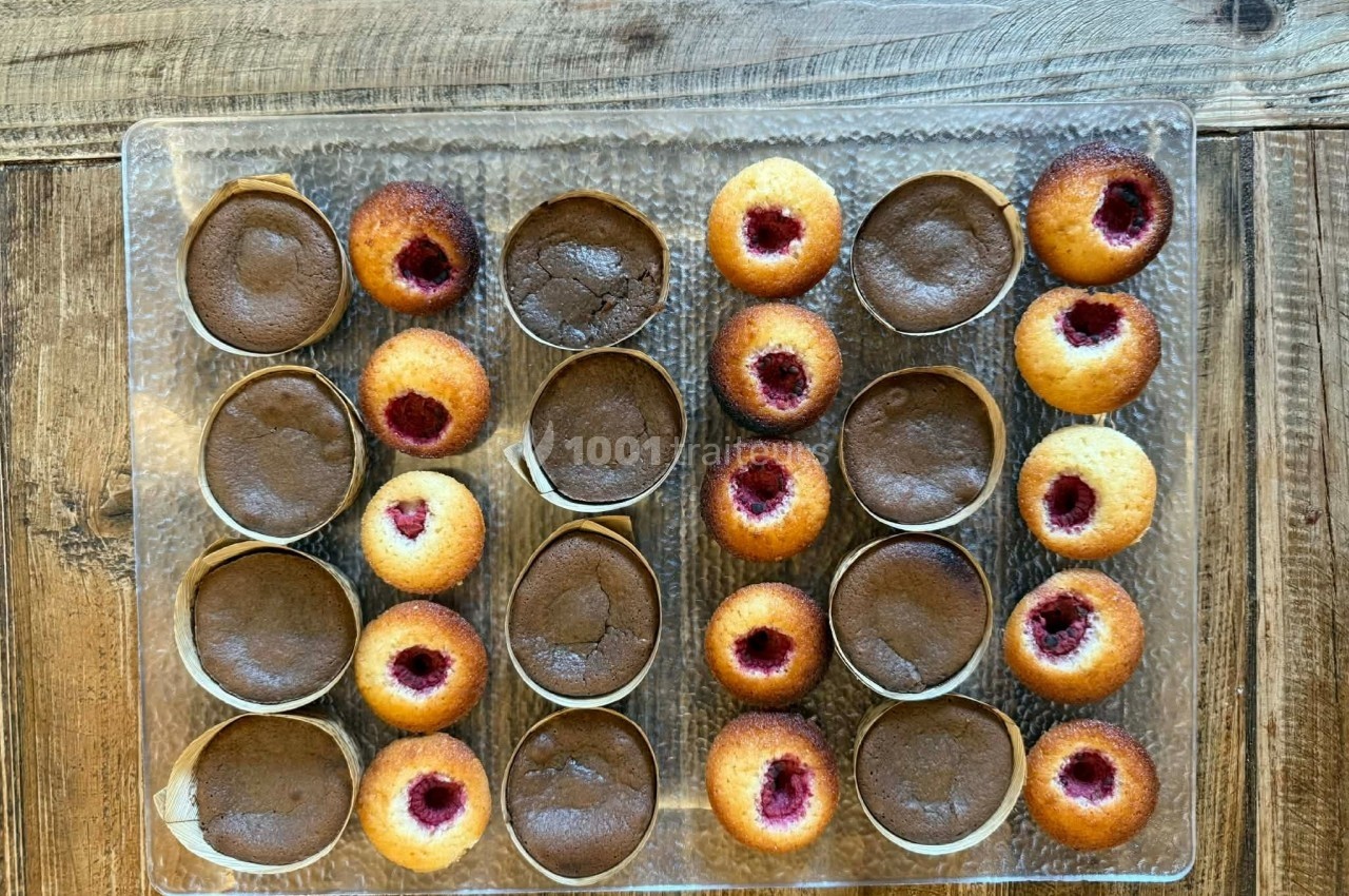 Plateau de petits gâteaux variés, incluant des moelleux au chocolat et des financiers à la framboise, sur une table en bois.