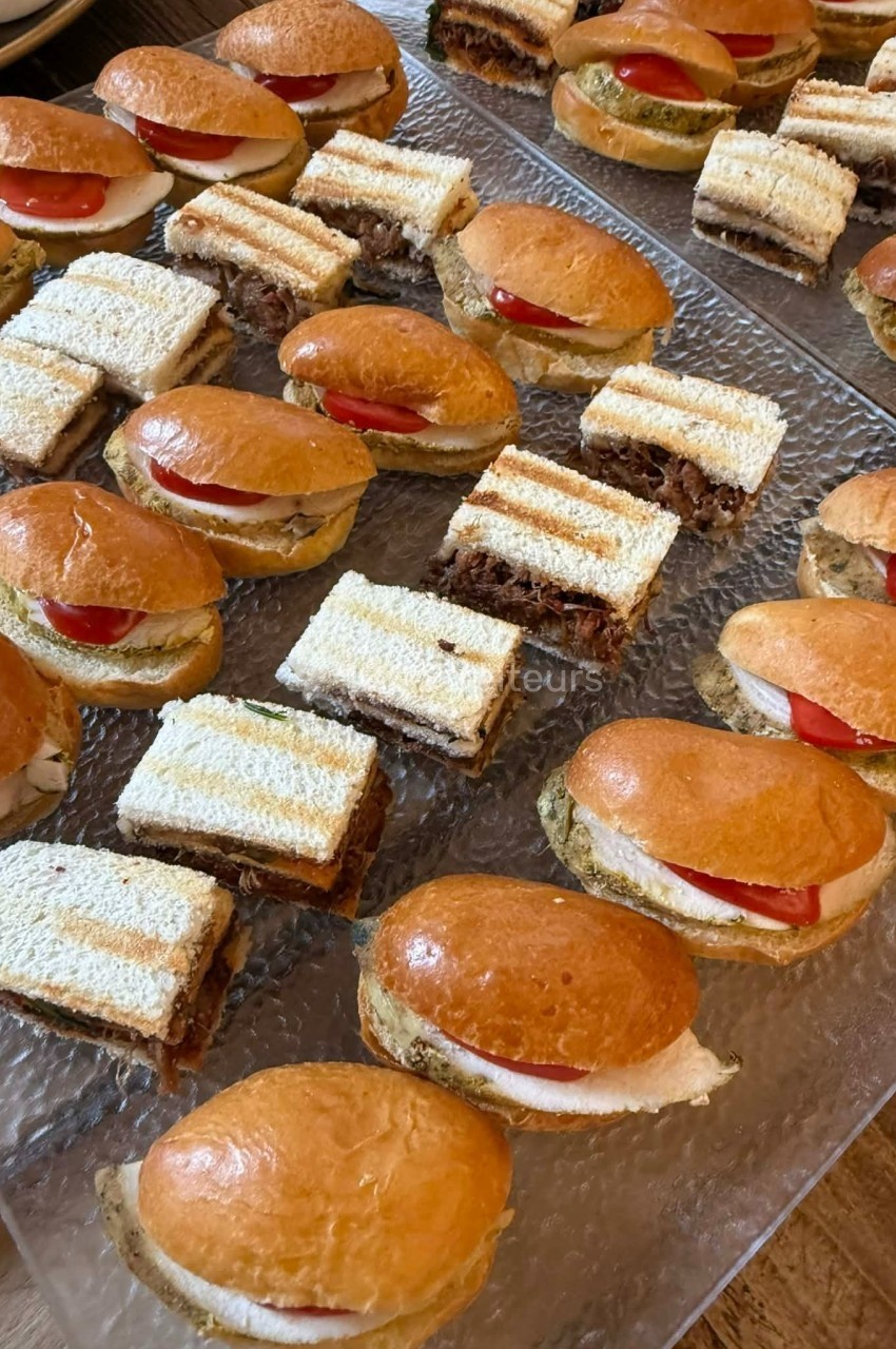 Plateau de mini-sandwichs variés, comprenant des pains briochés garnis et des tranches de pain de mie superposées.