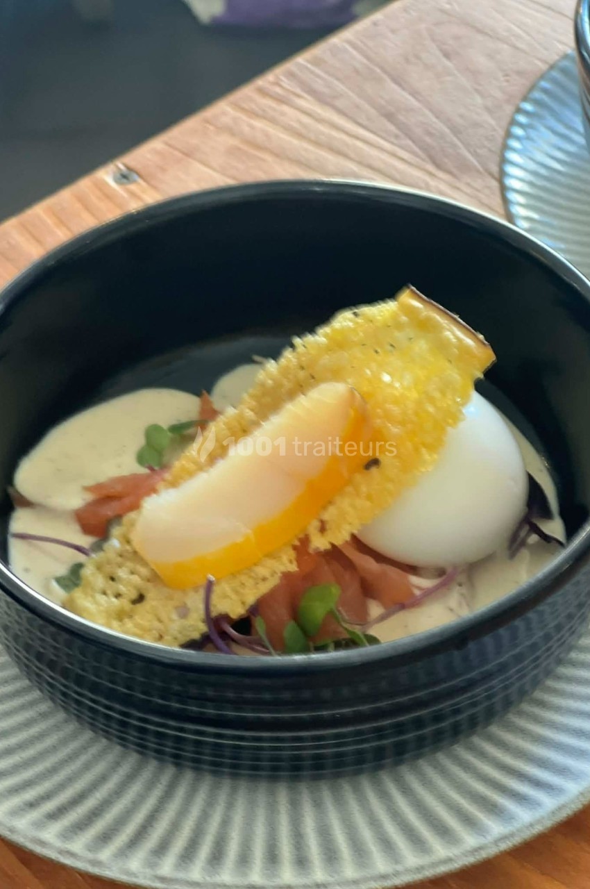 Œuf mollet avec saumon fumé, crème, jeunes pousses et tuile croustillante, présenté dans un bol noir.