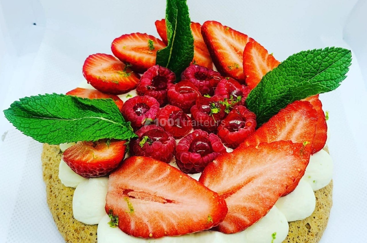 Tarte garnie de crème, fraises, framboises et feuilles de menthe, présentée sur un fond blanc.