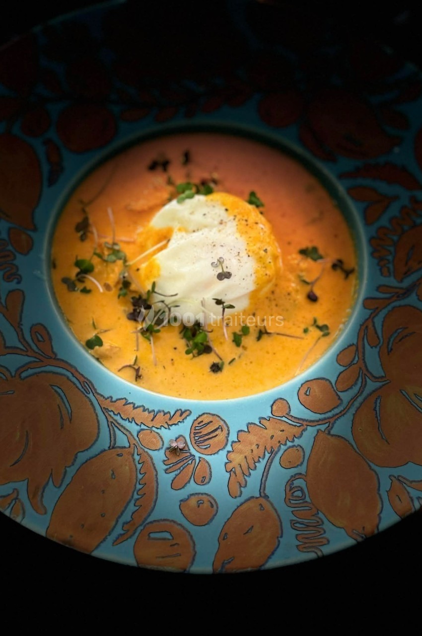Assiette décorée contenant une soupe orange garnie de crème, herbes fraîches et pousses.