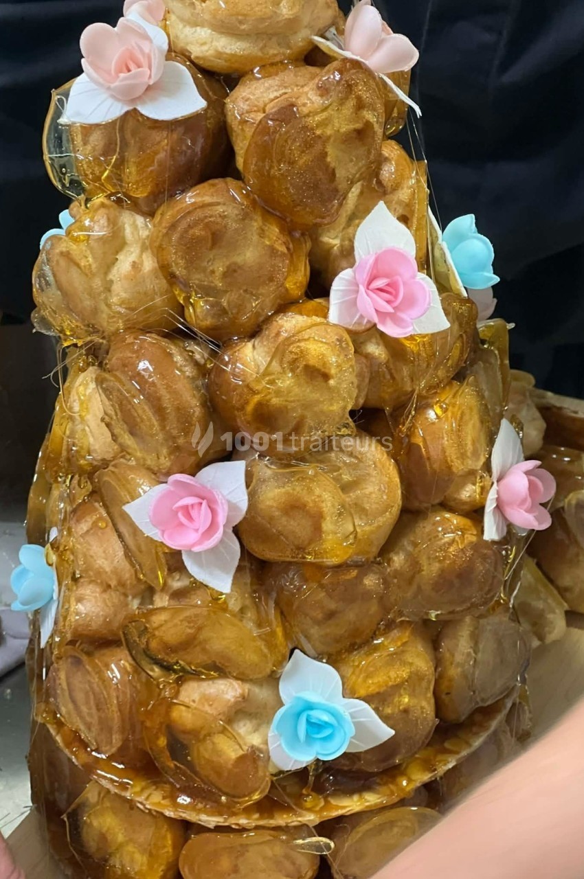 Tour de choux caramélisés décorée de fleurs en sucre roses et bleues, assemblée pour un dessert festif.