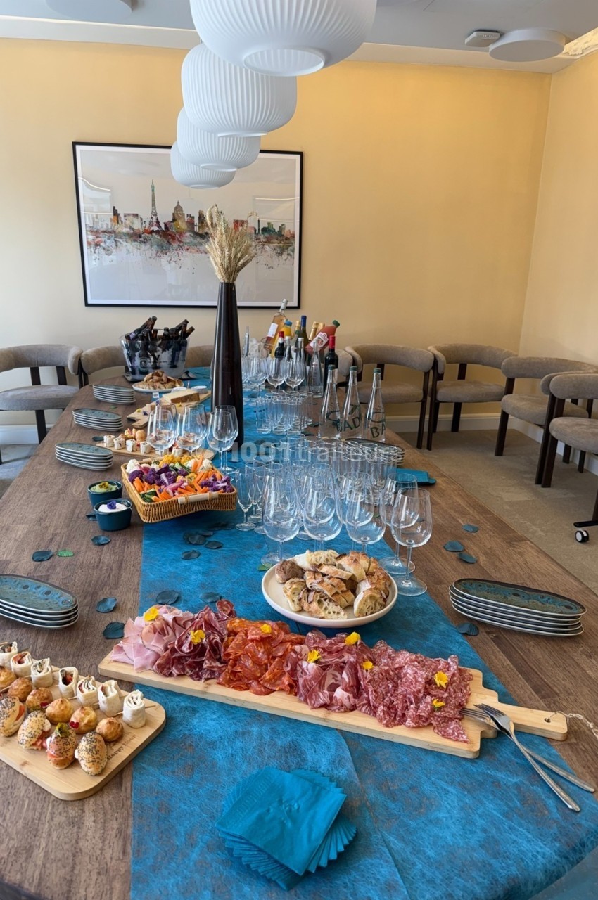 Table dressée avec planches de charcuterie, amuse-bouches, biscuits, verres et boissons dans une salle lumineuse.