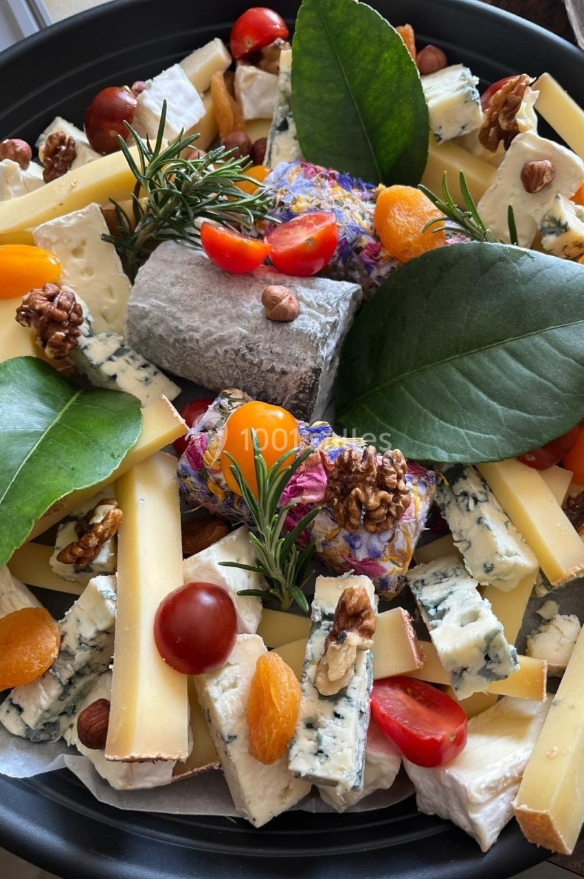 Plateau de fromages variés avec fruits secs, tomates cerises, abricots secs, herbes fraîches et feuilles décoratives.