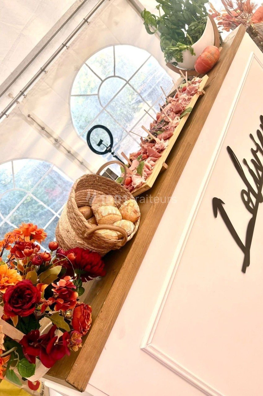 Plateau de charcuterie, panier de pain et décorations florales sur un comptoir en bois dans un espace lumineux.